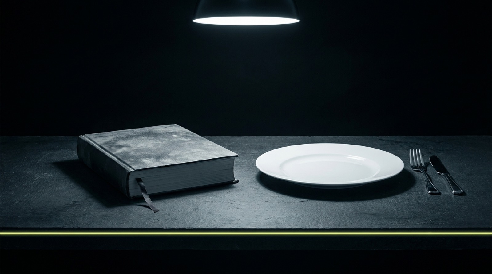 A thick dusty closed cookbook on a dark table beside a completely empty white dinner plate and clean cutlery.