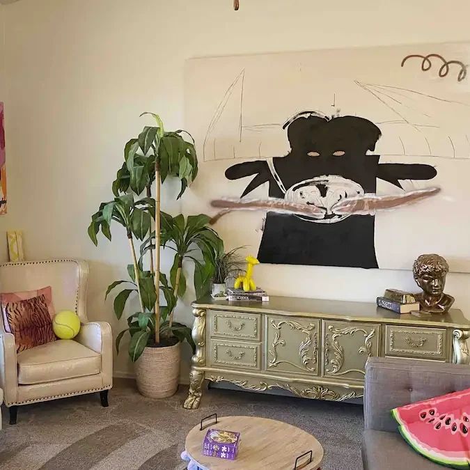 Living room with a large black-and-white painting, gold console and a watermelon rug