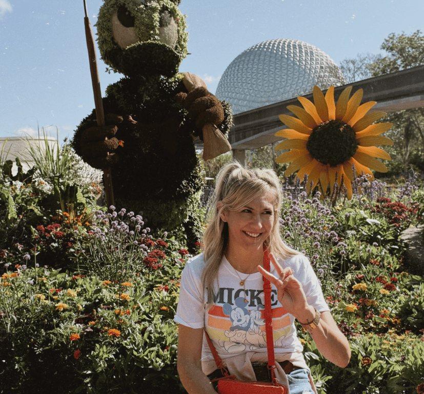 Tanina in a flower garden at Epcot, flashing a peace sign